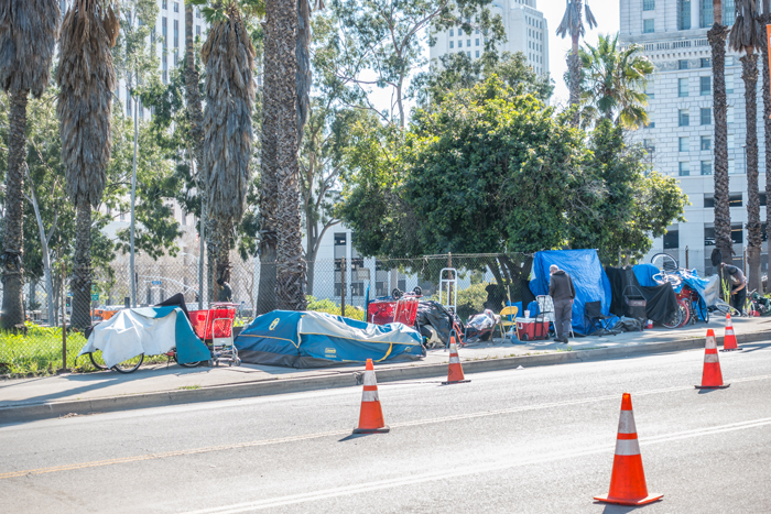 A photo showing a homeless encampment, including tents, bicycles, and personal belongings, on a sidewalk in Los Angeles.